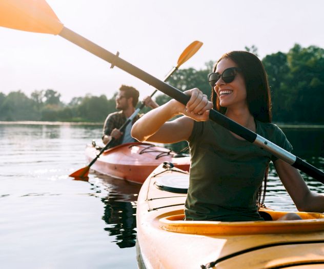 Two people are kayaking on a calm body of water, enjoying a sunny day outdoors.