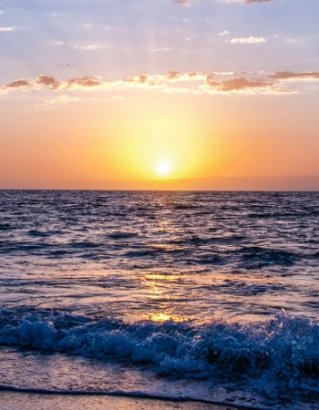 A stunning sunset over the ocean with waves gently crashing onto the shore, casting a warm glow across the water and sky.